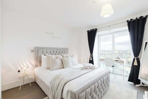 Ein Schlafzimmer mit einem großen Bett, einem Nachttisch mit Lampe, Blick auf die Stadt durch das Fenster und einem Balkon mit Stuhl.
