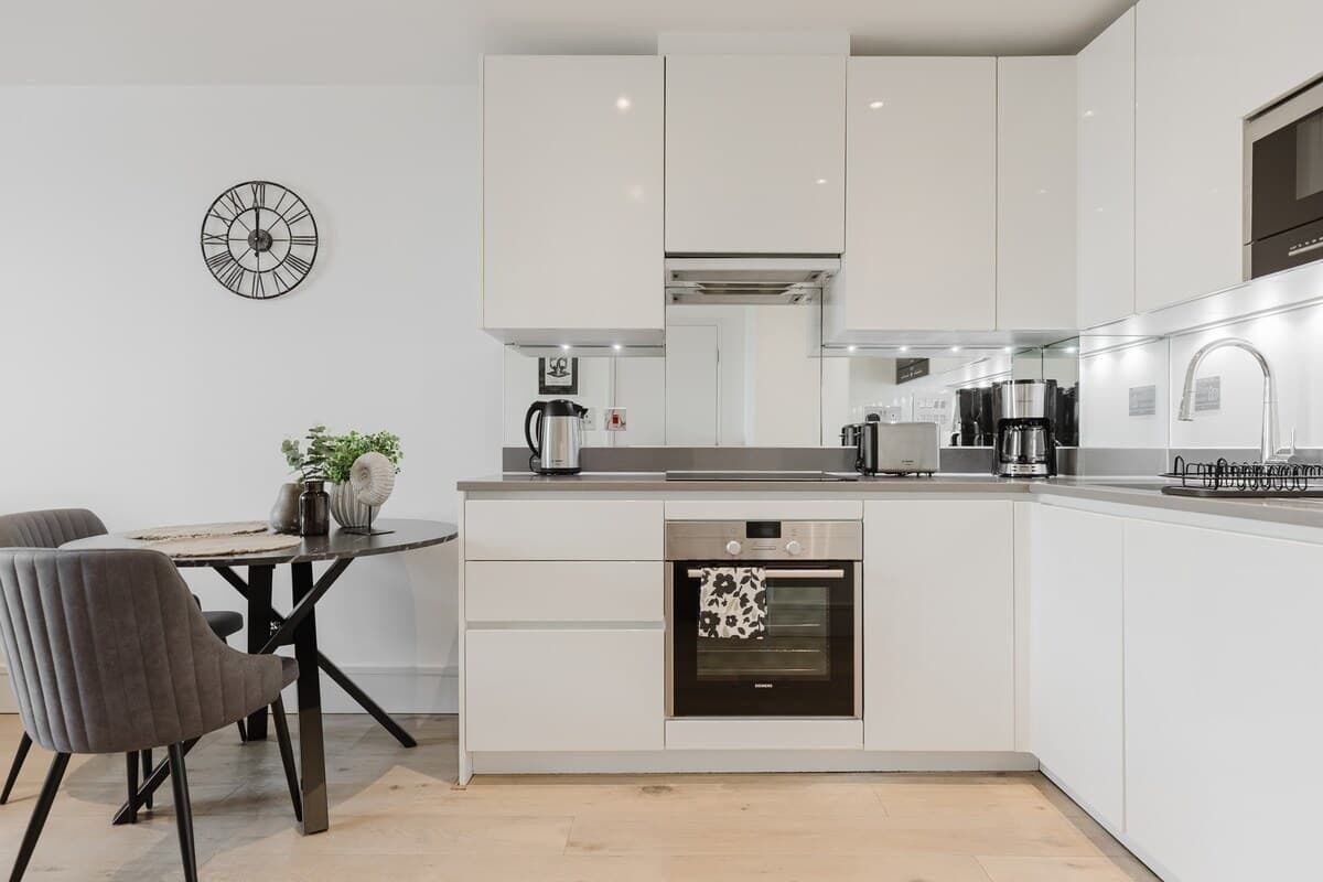 A modern kitchen with white cabinetry, a built-in oven, a coffee maker, and a clock on the wall.
