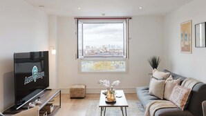 A modern living room with a television, a sofa, a coffee table, and a window with a city view. - Luxury 1BR w/City views & A/C - Clapham (Greater London)