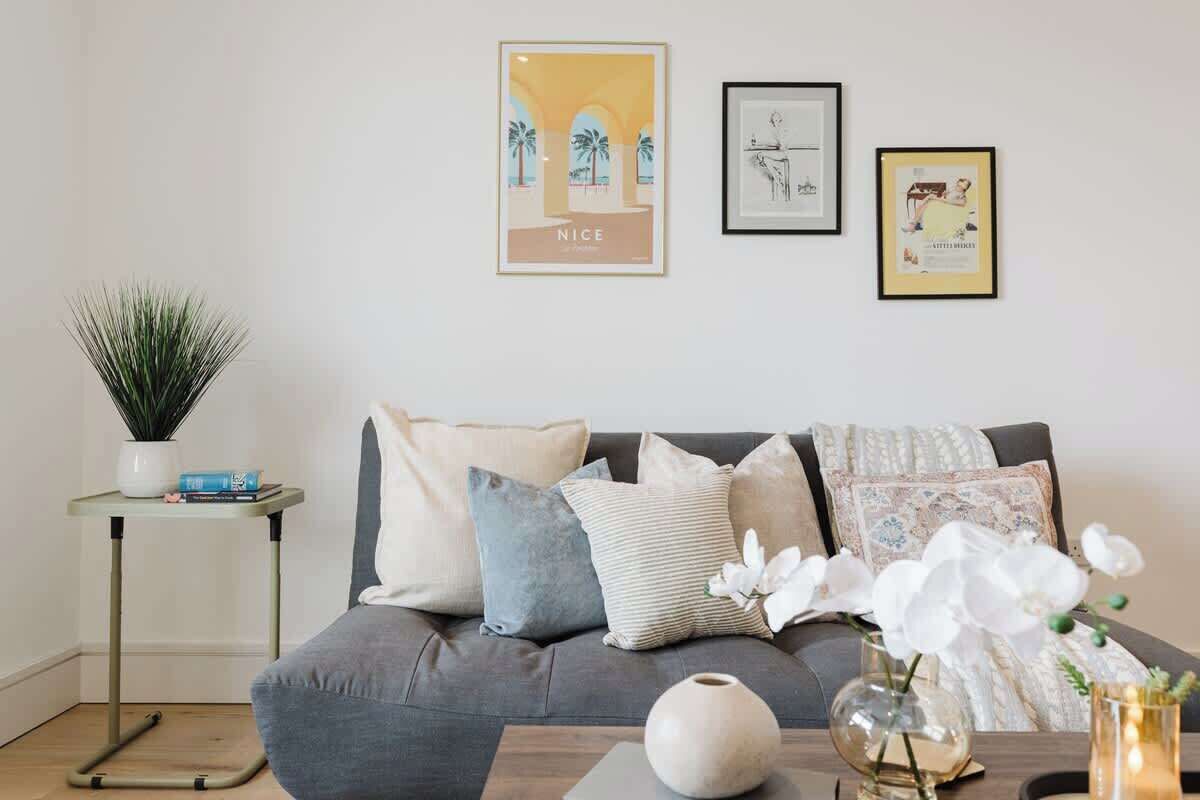 En moderne stue med en grå sofa, et lille sofabord, en potteplante og billeder på væggen.