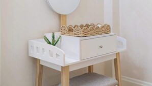 Une coiffeuse blanche avec un miroir rond, une petite plante et un cœur décoratif suspendu au mur.