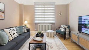 Un salon comprenant un canapé, une table basse, un pouf et un téléviseur.