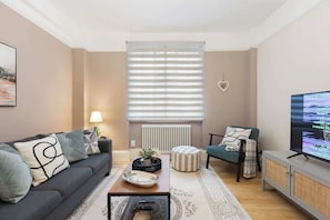 A living room with a sofa, coffee table, ottoman, and a television. - 2BR/BA-Ground Floor-Kensington (Greater London)