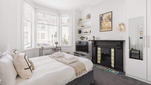 Een slaapkamer met een bed, een open haard, een televisie en een raam met jaloezieën.