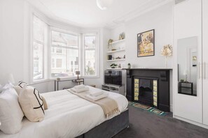 A bedroom with a bed, a fireplace, a TV, and a window with blinds. - Modern 2BR Kensal Rise Apartment, Wi‑Fi, Near Tube (Greater London)
