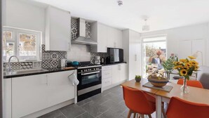 Een moderne keuken met witte kastjes, een zwarte kookplaat en een eethoek met oranje stoelen.