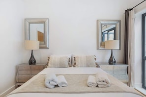 Une chambre d’hôtel bien rangée, avec un lit, deux tables de chevet, deux lampes et deux miroirs.