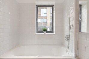 A modern bathroom with a bathtub, a window with a plant, and a shower area.