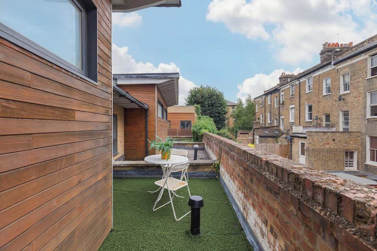 A modern building with a wooden exterior, a small patio with a table and chairs, and a brick wall.