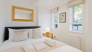 Hotellihuone, jossa on sänky, yöpöytä lampun kanssa, ikkuna, josta on näkymä, ja peili seinällä.