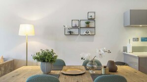 Uma sala de jantar com uma mesa de madeira, cadeiras, uma luminária e prateleiras fixadas na parede com objetos decorativos.