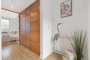 Ein Zimmer mit einem Holzschrank, einem gerahmten Bild an der Wand, einer Stehlampe und einem Korbwäschesammler.