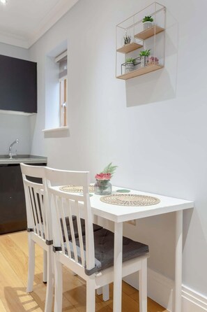 A white dining table with two chairs, a small potted plant, and a vase with flowers. - Delightful 1Bed-Private Patio-FR Parking-PingPong (Greater London)