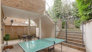 A ping pong table in an outdoor patio area with a brick wall, wooden fence, and a metal gate. - Delightful 1Bed-Private Patio-FR Parking-PingPong (Greater London)