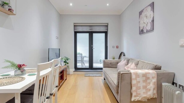 A modern living room with a sofa, a dining table with chairs, a TV, and a large window with a view. - Delightful 1Bed-Private Patio-FR Parking-PingPong (Greater London)