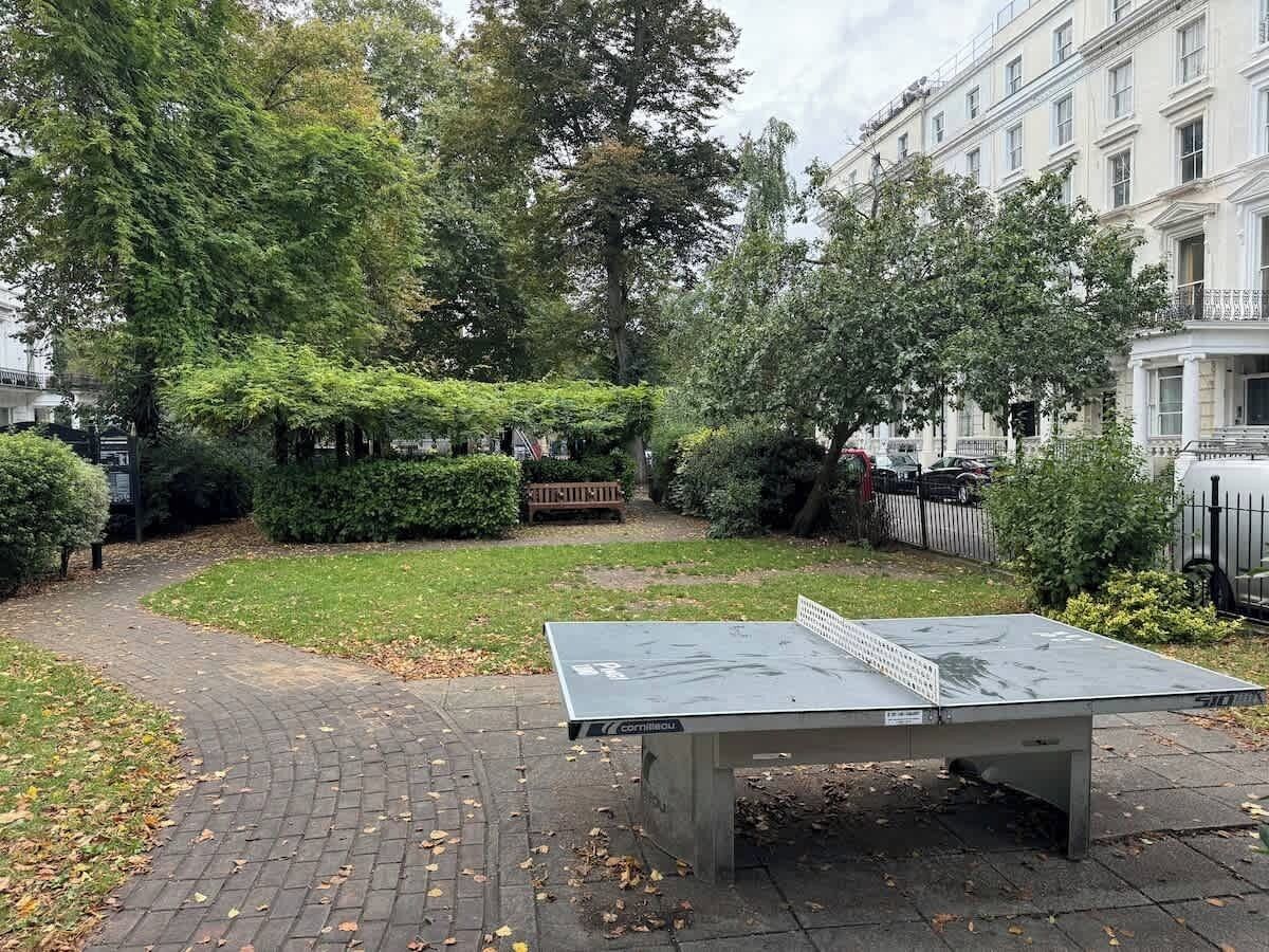 A courtyard with a ping pong table, surrounded by greenery and a brick pathway.