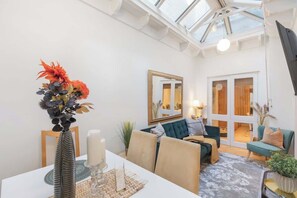 Ein Zimmer mit Esstisch, Stühlen, einer Couch, einem Spiegel und Blick durch eine Glastür.