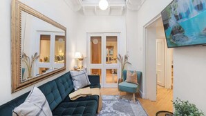 En stue med en mørkegrøn sofa, en skiferfarvet lænestol, et stort spejl og et fjernsyn, der viser et vandfald.