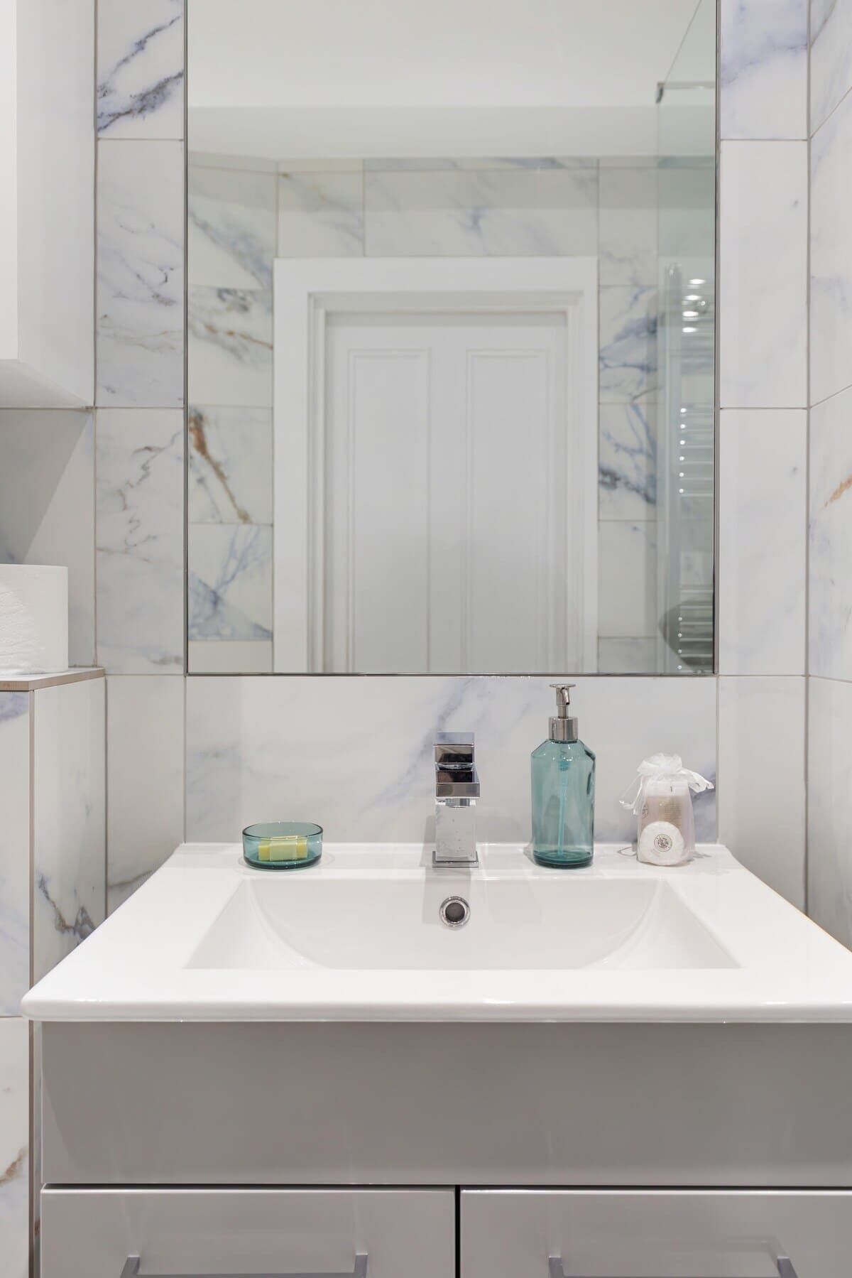 Een badkamer met een witte wastafel, een spiegel en een betegelde muur van marmer.