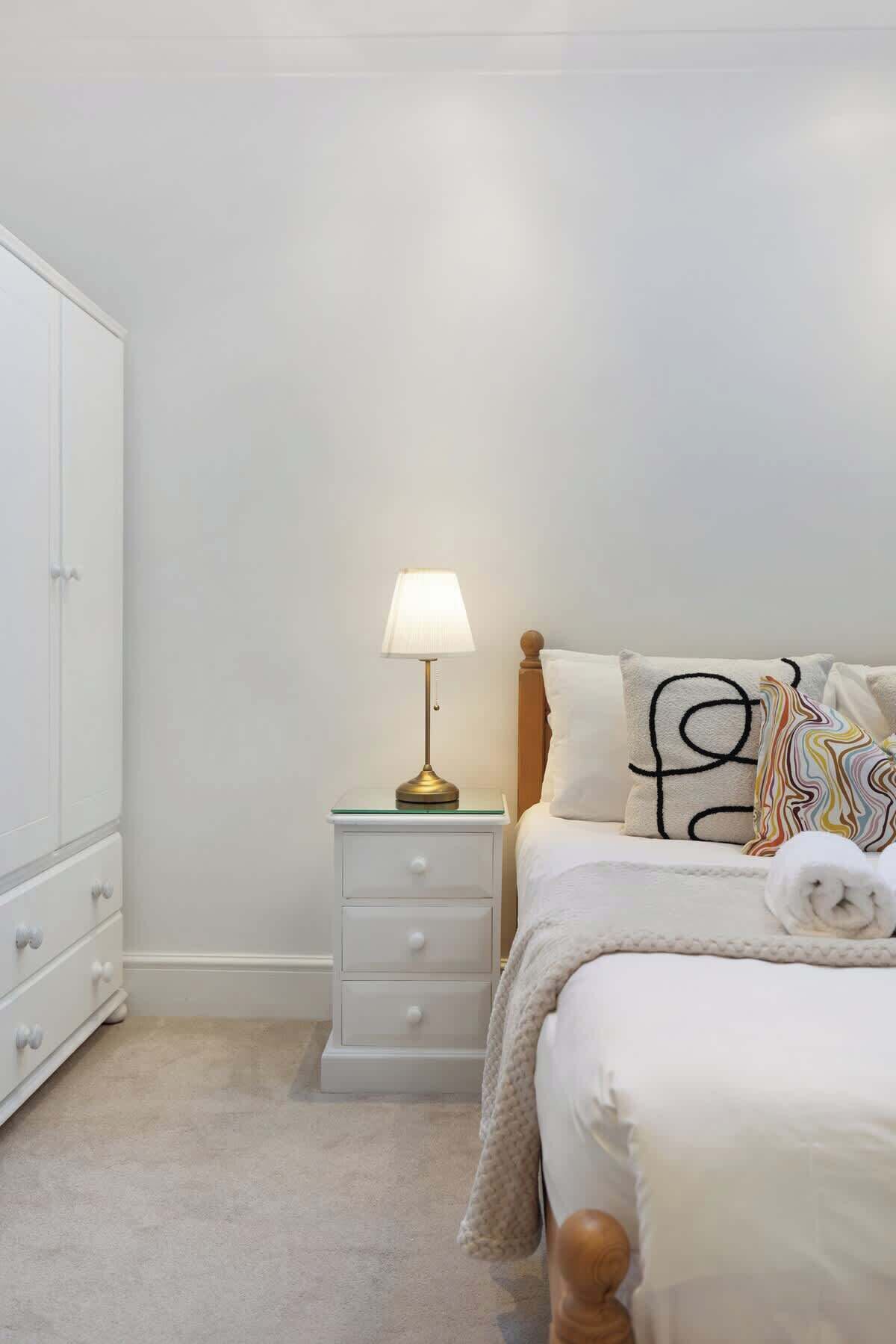 Een slaapkamer met een bed, een nachtkastje met een lamp, een dressoir en een kast.