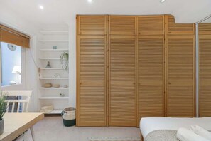 Ein Schlafzimmer mit einem Bett, einem Holzschrank, einer weißen Regaleinheit und einem Fenster mit Jalousien.
