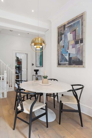 Un coin repas avec une table ronde, des chaises noires, une suspension et un grand tableau abstrait accroché au mur.