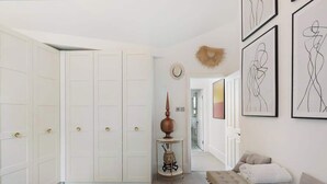 Un pasillo con puertas blancas, una pequeña mesa con un florero y obras de arte en la pared.