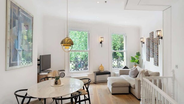 Una sala de estar moderna con comedor, ventanas amplias, un sofá blanco y una araña.