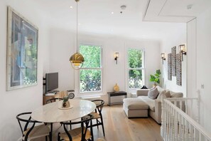 Un salon moderne comprenant un coin repas, de grandes fenêtres, un canapé blanc et un lustre.