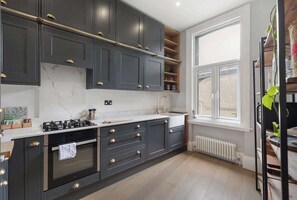 Une cuisine moderne avec des meubles de couleur sombre, un plan de travail blanc et une fenêtre qui laisse entrer la lumière naturelle.
