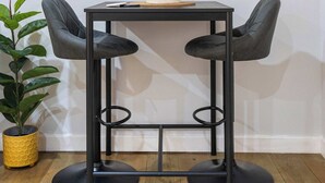 Een moderne kamer met een zwart metalen tafeltje, twee stoelen, een ronde spiegel en een potplant.