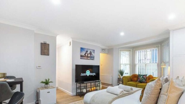 Een woonkamer met een flatscreen-televisie, een bank, een eettafel en een kleine plant.