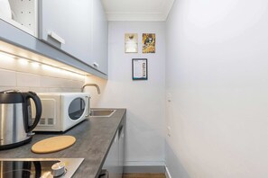 Une cuisine compacte équipée d’une bouilloire, d’un four à micro-ondes et d’un grille-pain sur le plan de travail, d’un petit évier et d’un tapis en liège.