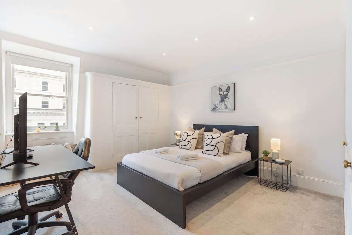 A bedroom with a bed, bedside table, lamp, and a window.