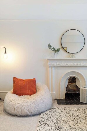 A room with a white fluffy ottoman, a fireplace, a round mirror, and a light fixture. - Stunning 2BR - South Kensington (Greater London)