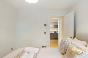 A hotel room with a bed, pillows, a bedside table, and a view into the kitchen area. - Gorgeous 2BR2BA w Balcony & AC Clapham North (Greater London)