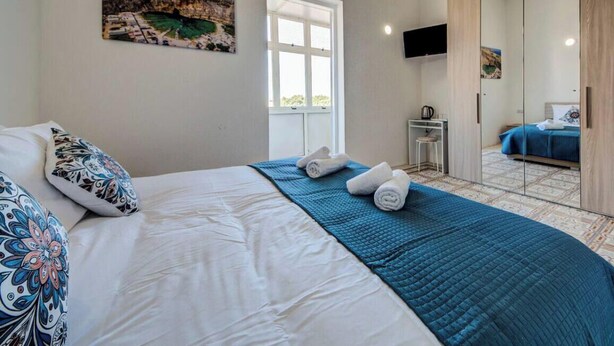Quarto com cama, escrivaninha, cadeira e televisão.
