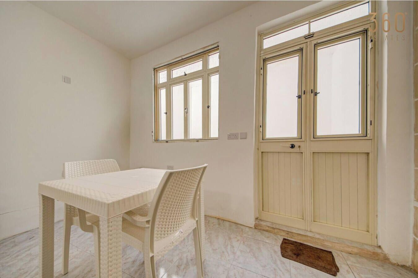 Una habitación con una mesa y sillas blancas, dos ventanas y una puerta.