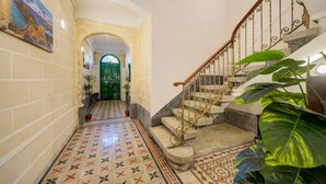 Um corredor com piso ladrilhado, escada com corrimão de metal e uma porta verde no final.