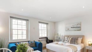 A modern bedroom with a bed, a blue sofa, and a radiator. - Luxe 1BD + A/C | King Bed & 75" TV | Notting Hill (Greater London)