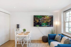 Ett modernt vardagsrum med en matplats, en blå soffa och en tv-skärm som visar ett naturbild.