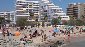 Ein Strand mit Menschen, Zelten und Gebäuden im Hintergrund.