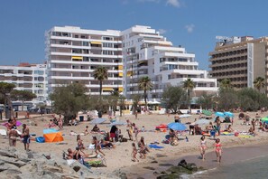 Ein Strand mit Menschen, Zelten und Gebäuden im Hintergrund.