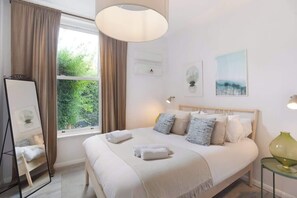 A hotel room with a bed, a mirror, a window with curtains, a lamp, and artwork on the wall. - Heartwarming Newly Renovated 1BR w/Patio - Clapham (Greater London)