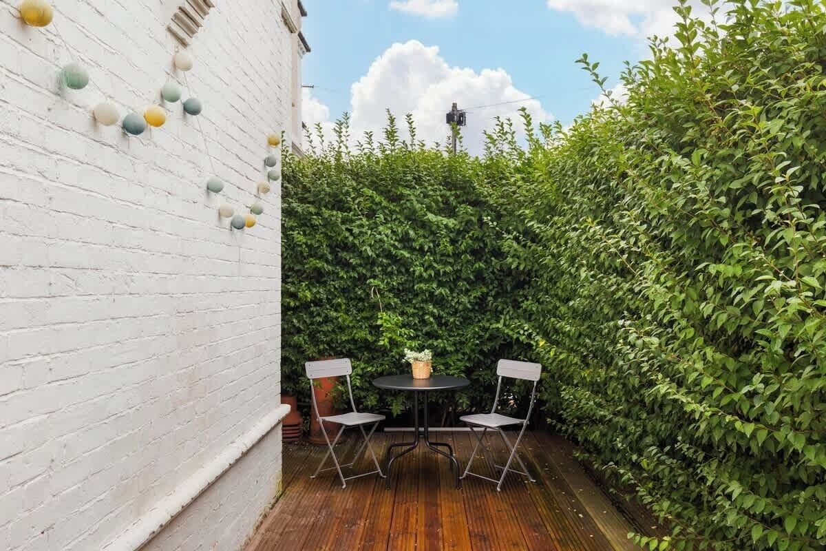 A patio with a round table and two chairs, surrounded by a white brick wall and a hedge.