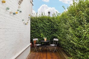 A patio with a round table and two chairs, surrounded by a white brick wall and a hedge. - Heartwarming Newly Renovated 1BR w/Patio - Clapham (Greater London)