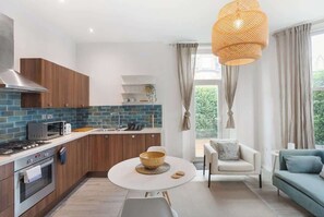 A modern kitchen with a dining area, a sofa, and a view of greenery. - Heartwarming Newly Renovated 1BR w/Patio - Clapham (Greater London)