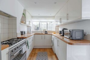A compact kitchen with white cabinets, a gas stove, a microwave, and a washing machine. - 3BR House W/Patio Queens Park (Greater London)