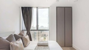 Un dormitorio moderno con un ventanal grande, una cama con almohadas, una mesita de noche y un armario.