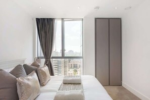 Ein modernes Schlafzimmer mit großem Fenster, einem Bett mit Kissen, einem Nachttisch und einem Kleiderschrank.